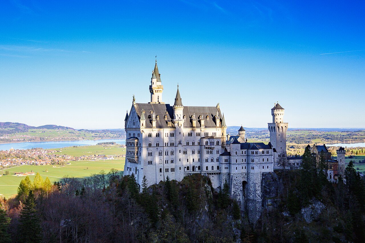 Neuschwanstein Castle on its wooded hilltop with Bavarian lakes and countryside beyond